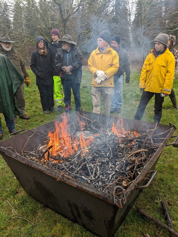 people are standing around a firepit with materials burning to make biochar as part of a demonstration