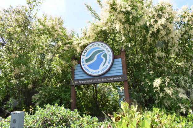 photo of the EMSWCD office sign with logo mounted on a board, framed by oceanspray bushes behind the sign