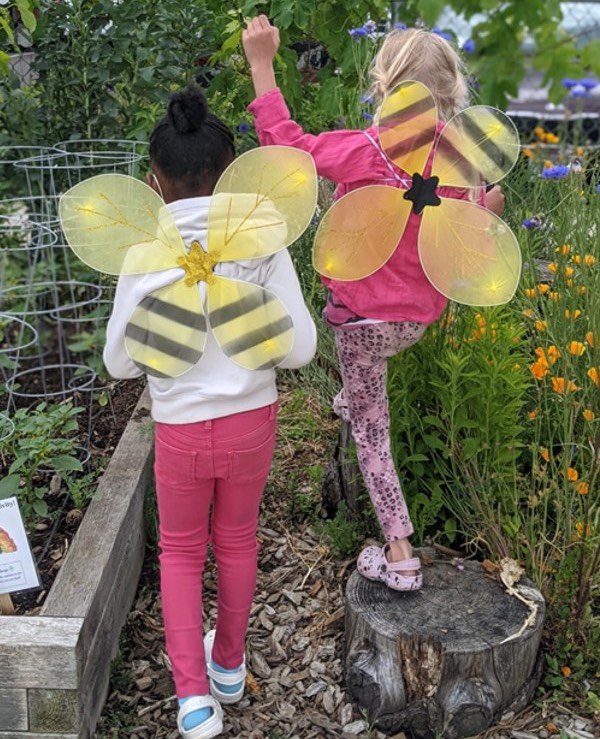 Two young girls wearing bee costumes in a garden