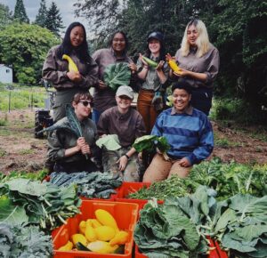 A group of young people smile and hold vegetables with more harvested crops in the foreground.