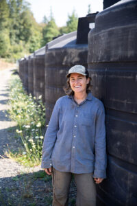 Kate Coppoletta standing in front of several large rain harvesting tanks